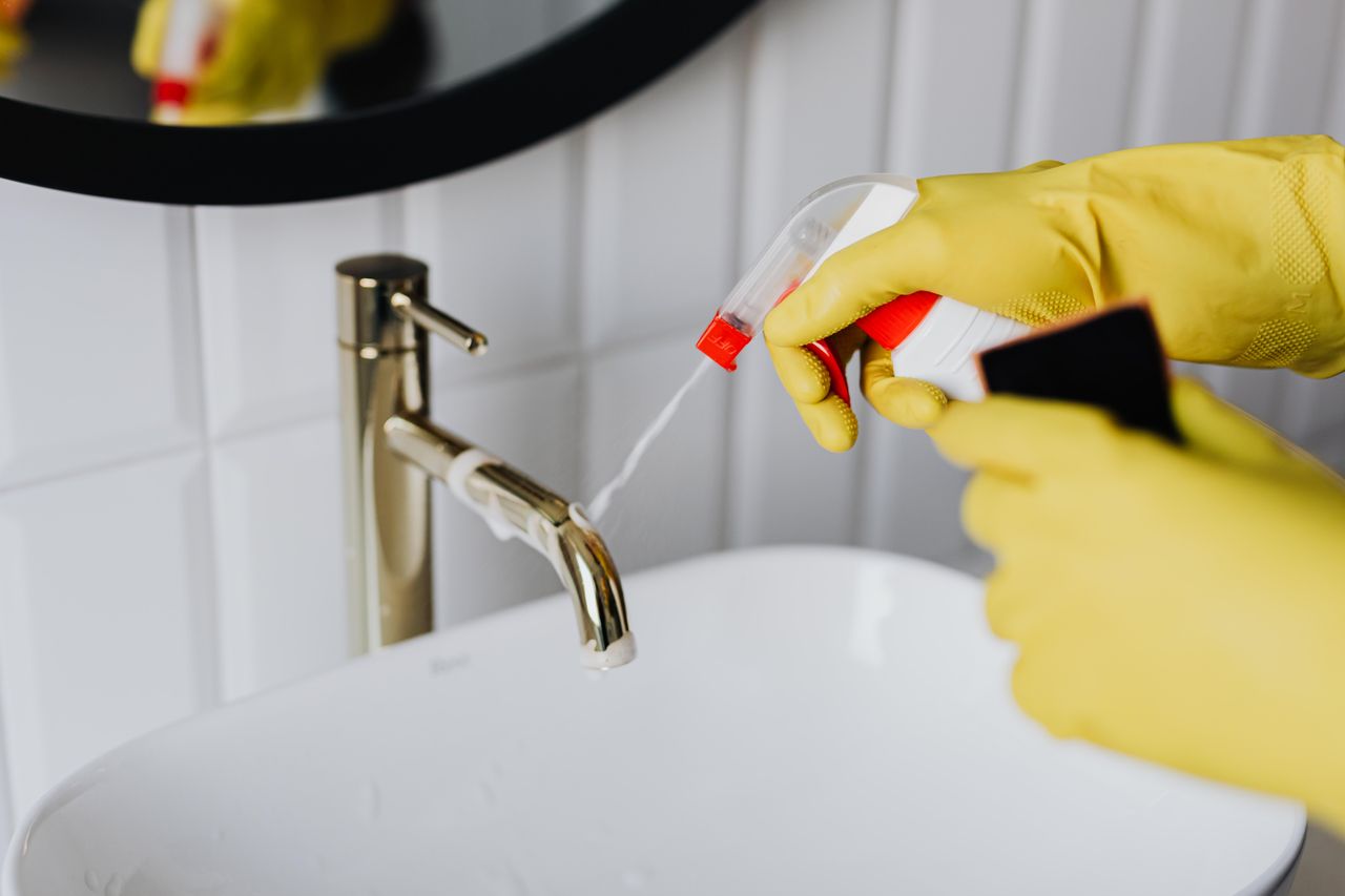 creative-02 From above anonymous housekeeper in yellow rubber gloves spraying cleaner to chrome water faucet in bathroom