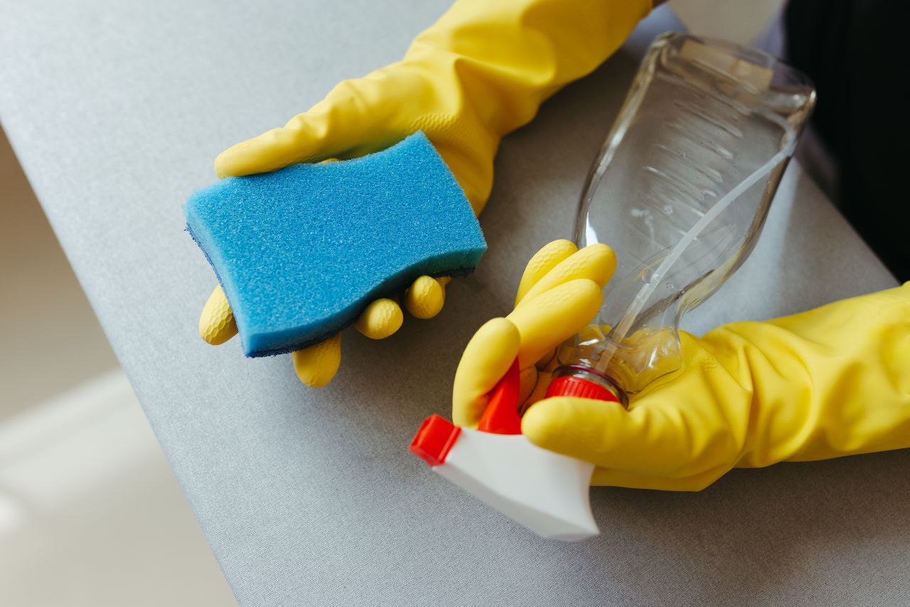 Services-01 Close-up of hands in gloves holding a sponge and spray bottle for cleaning.